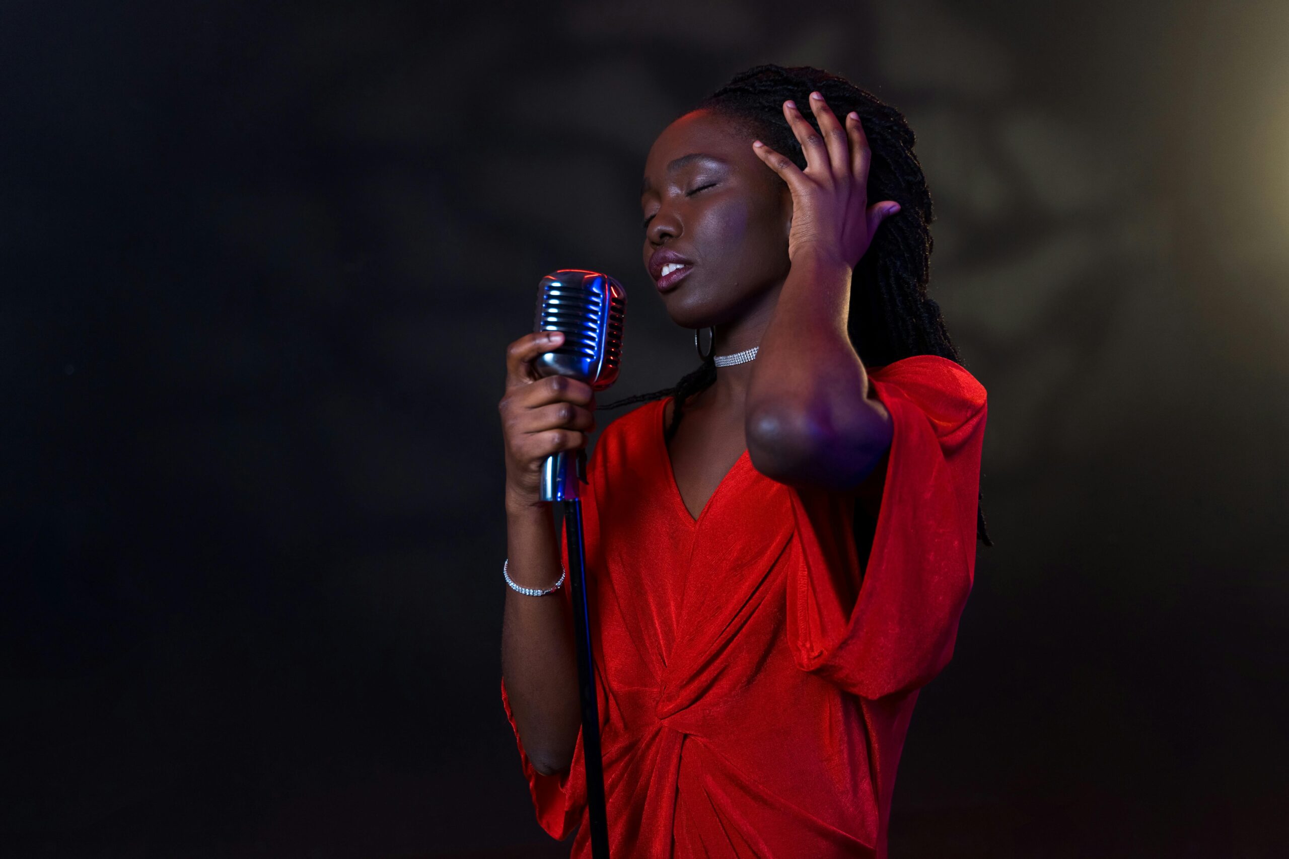 A black woman in a red dress passionately singing into a vintage microphone.